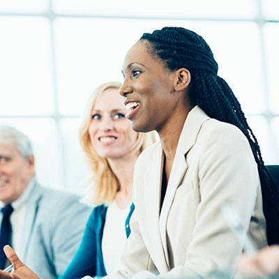 Smiling businesswoman in white blazer with colleagues in bright office setting during meeting or presentation.