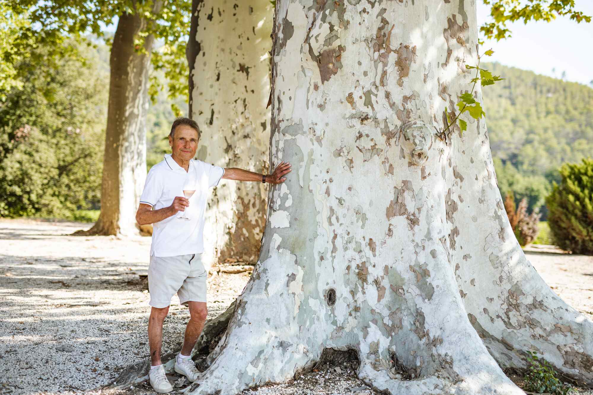 Winemaker Monsieur Xavier Paul stands leaning beside a tree with a glass in hand