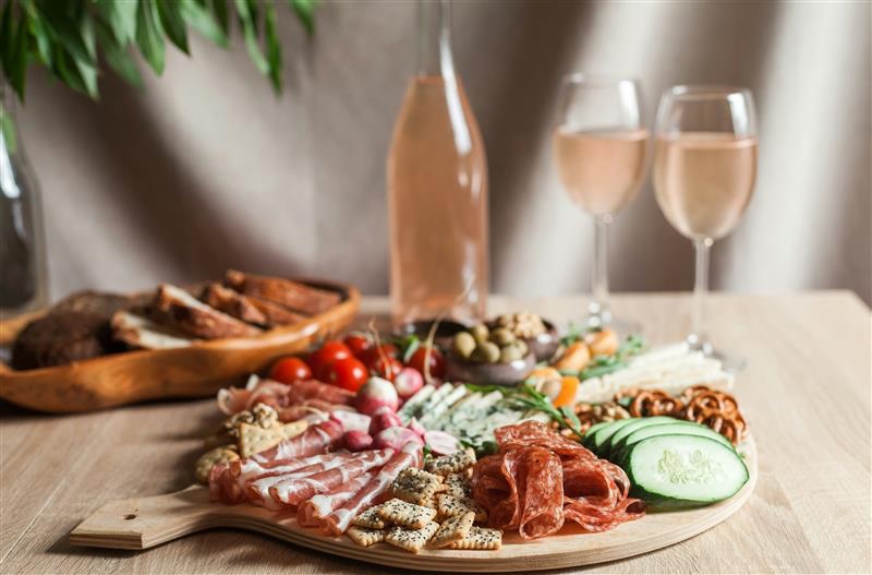 A ham and cheese platter with two glasses of rosé