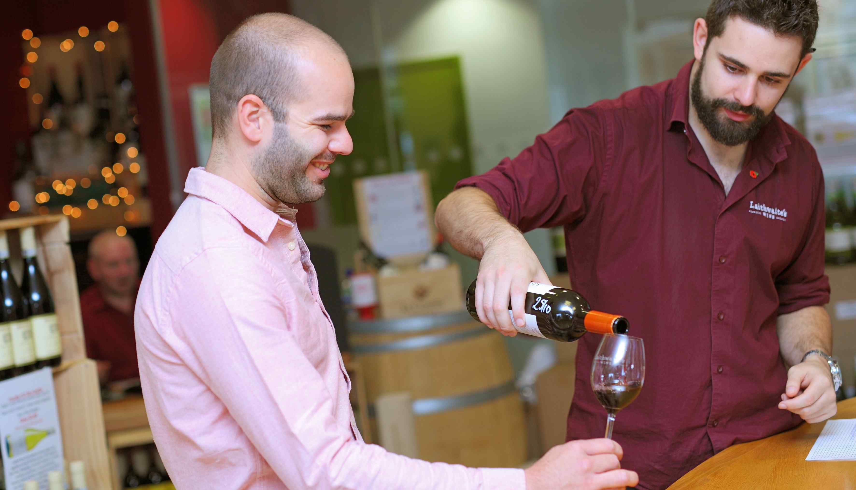 aithwaites shirt with beard pouring wine for another man in a pink shirt