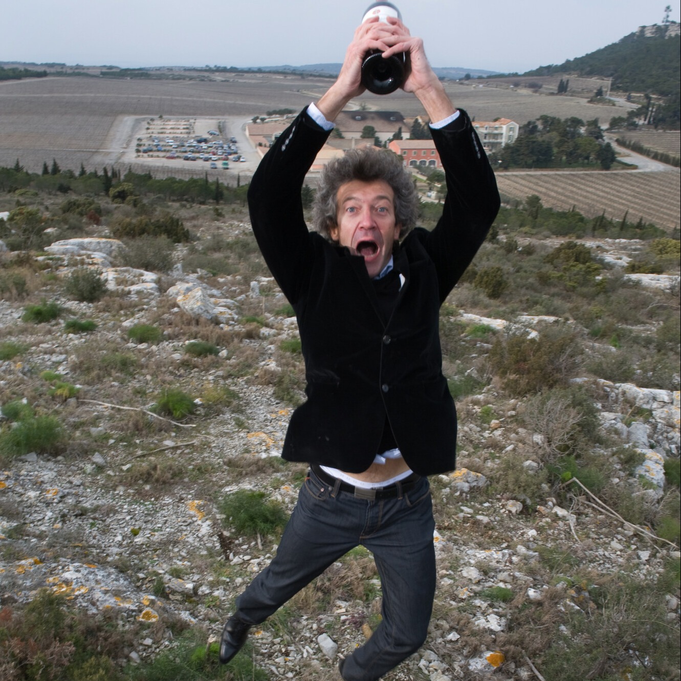 Winemaker Gérard Bertrand leaps into the air holding a bottle of red wine above his head