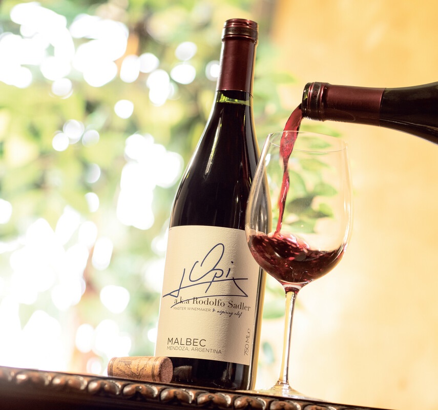 Red wine being poured into glass next to bottle of Opi Malbec