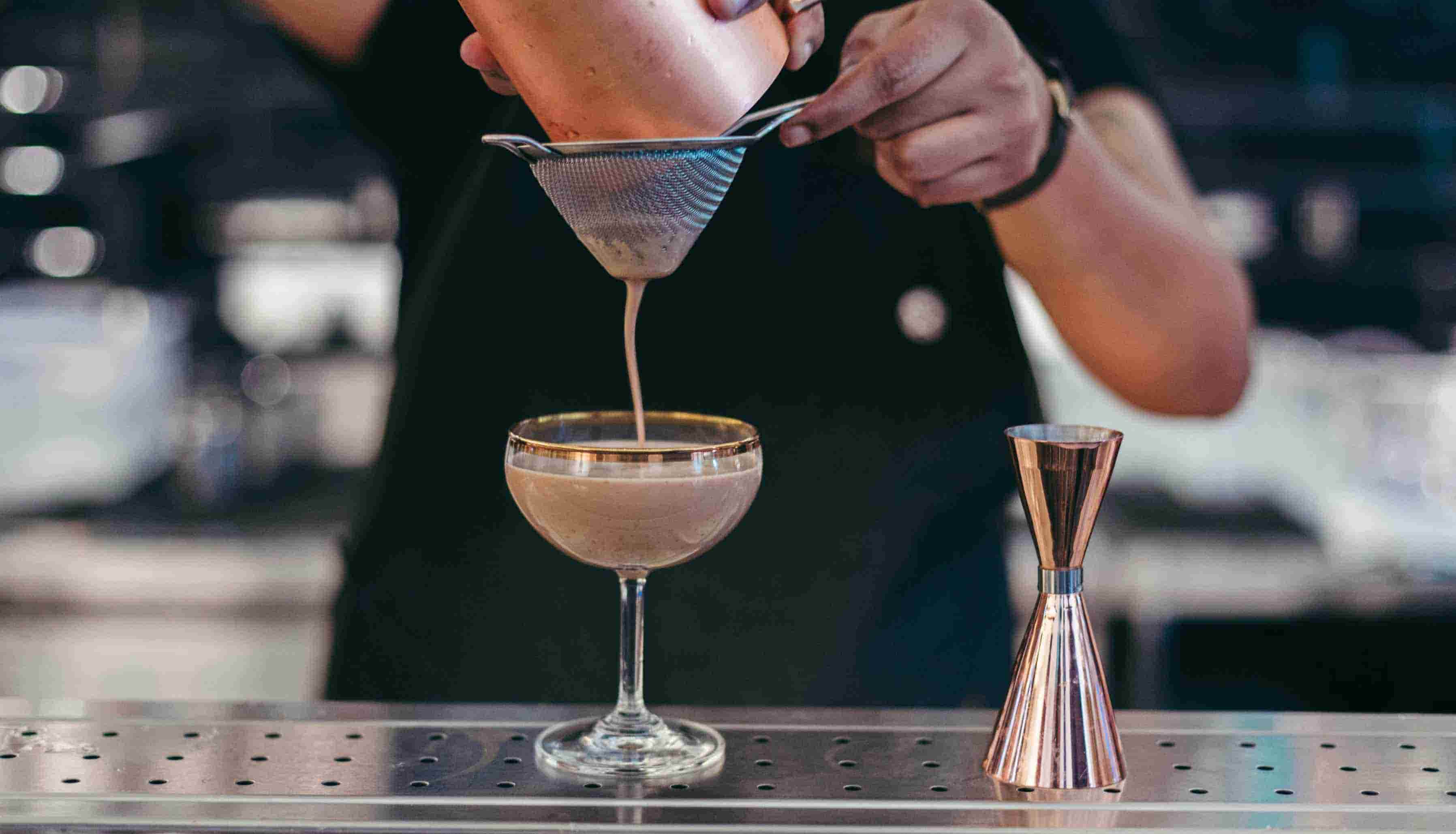 A barman straining a Nutty Irishman cocktail into a glass