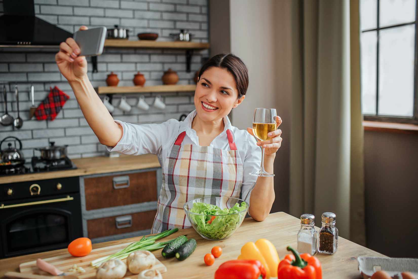 Woman in kitchen taking selfie with wine