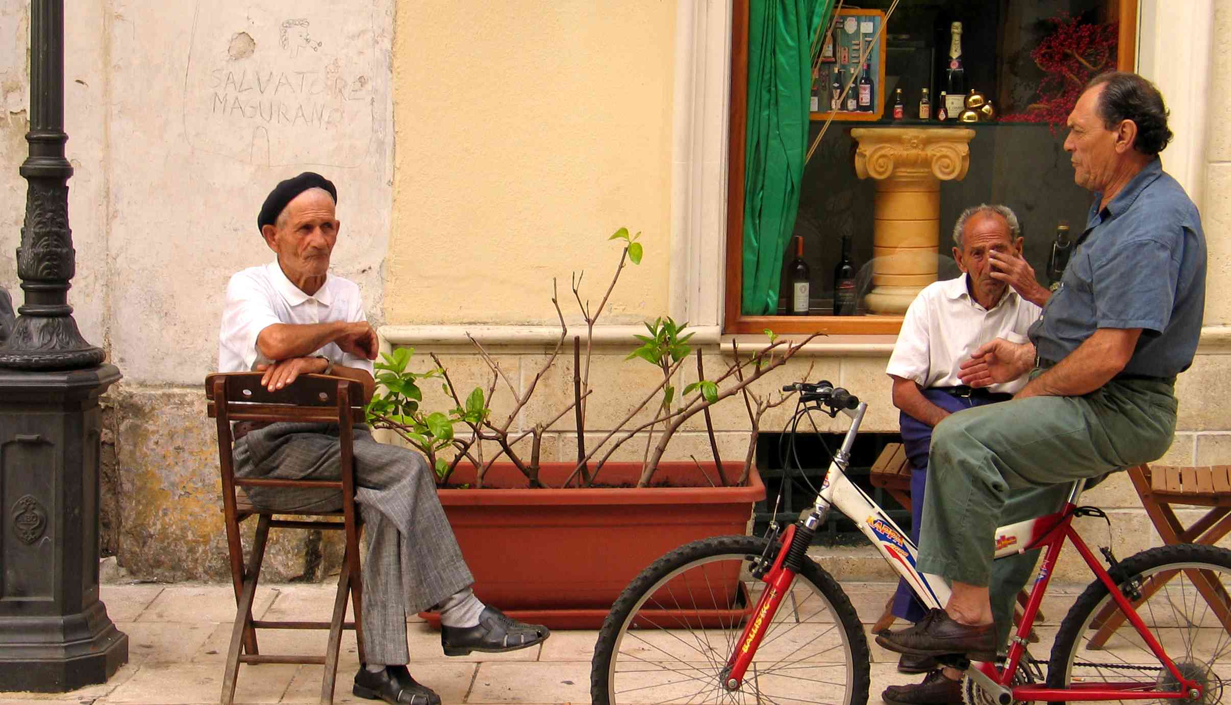 Three men in outside a bar in Puglia – two seated and one on a bycicle