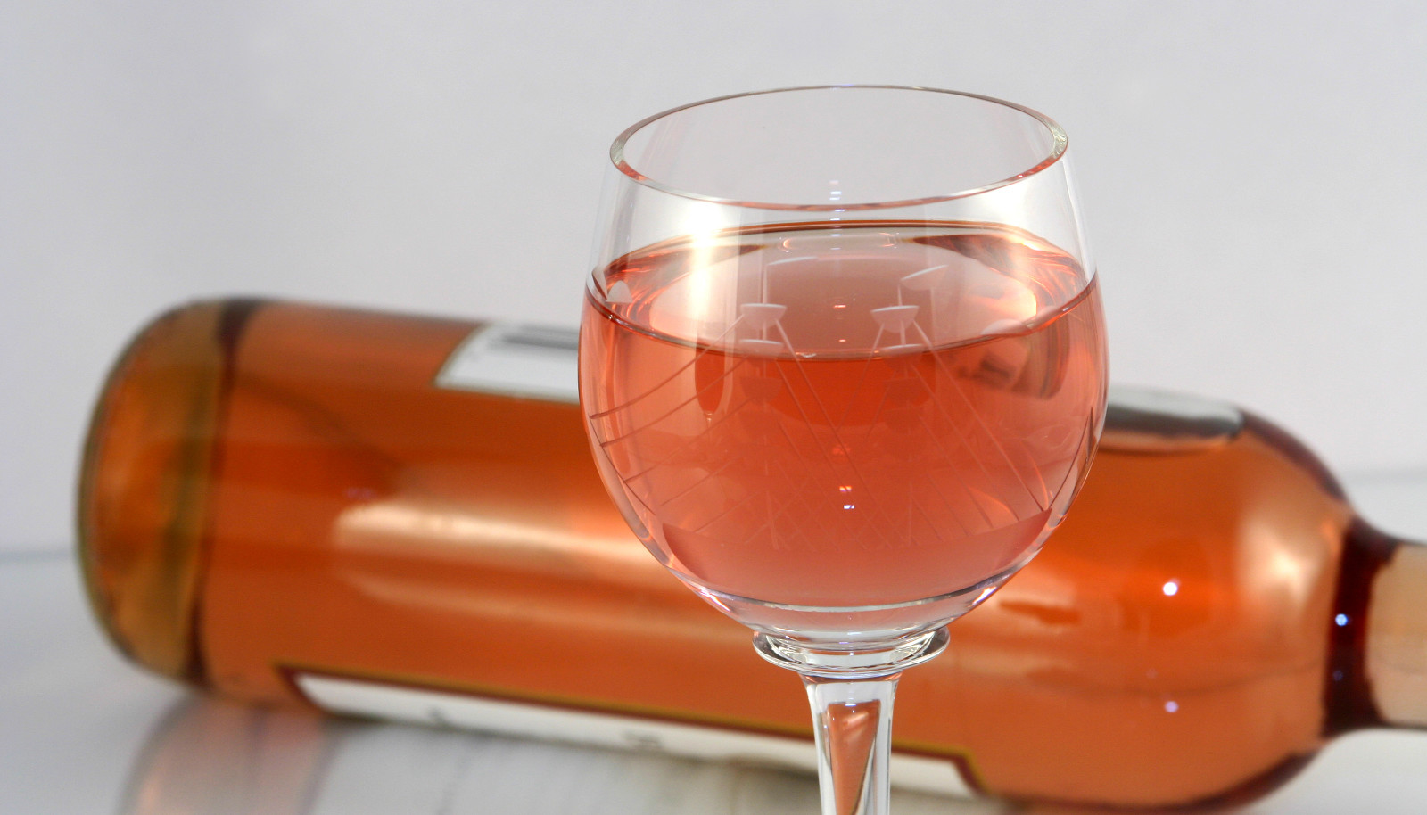 A glass of white Zinfandel wine with a bottle laying on its side behind it - Zinfandel wine