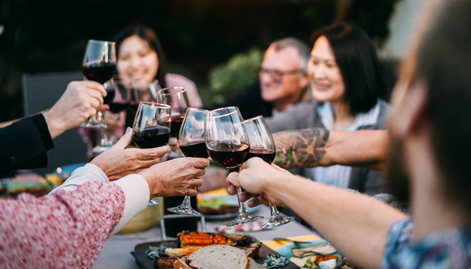 A group of friends celebrating around a dinner table raising glasses of red wine - Zinfandel wine