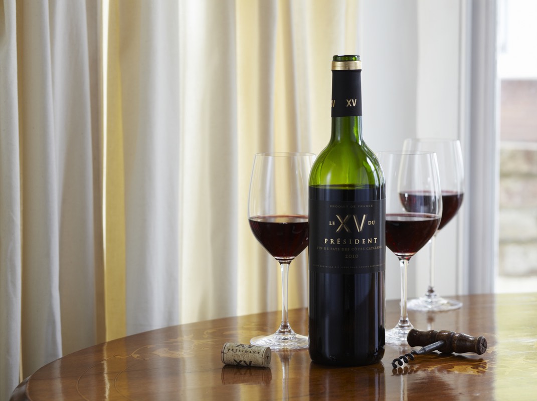 A bottle of Le XV Du President poured into three glasses with corkscrew and cork on a table