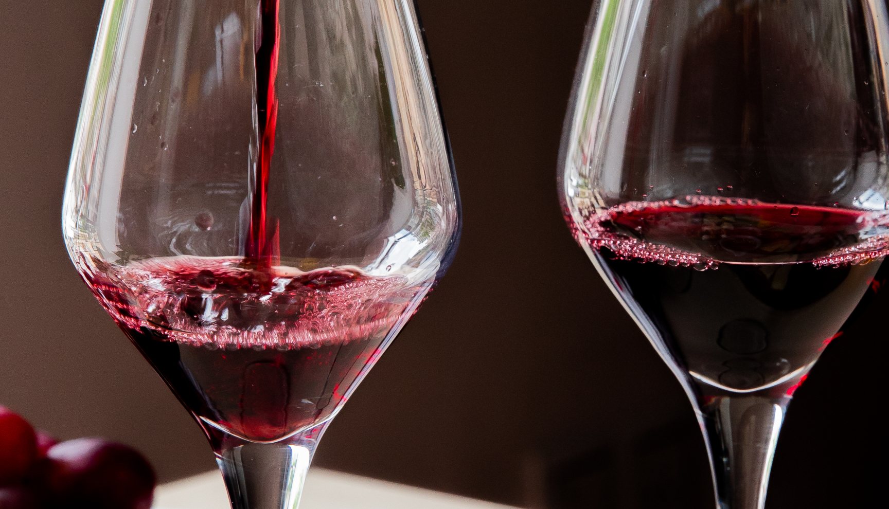 Hand pouring red wine into glass on table with cheeses