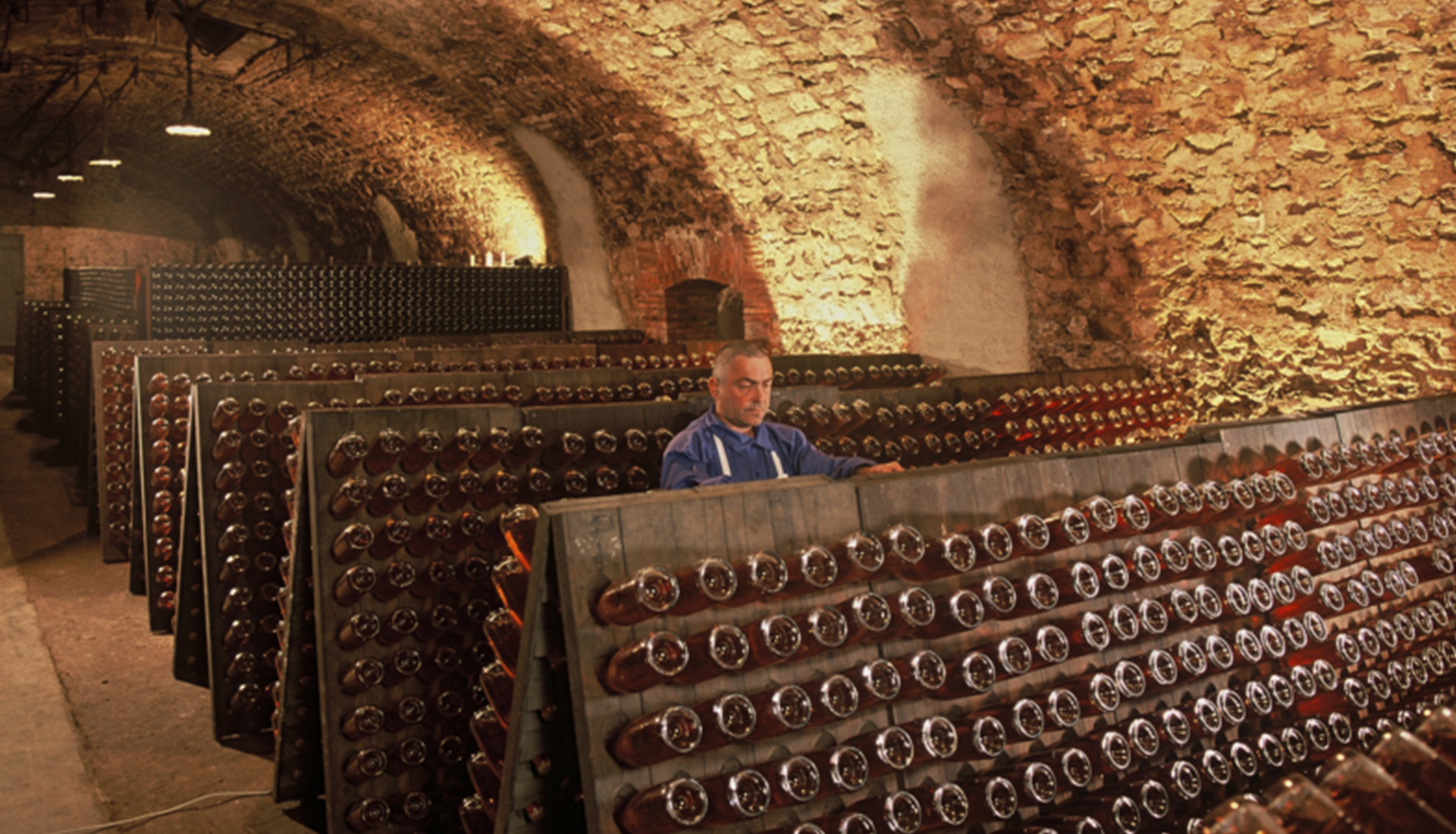 winemaker in wine cellar filled with bottles