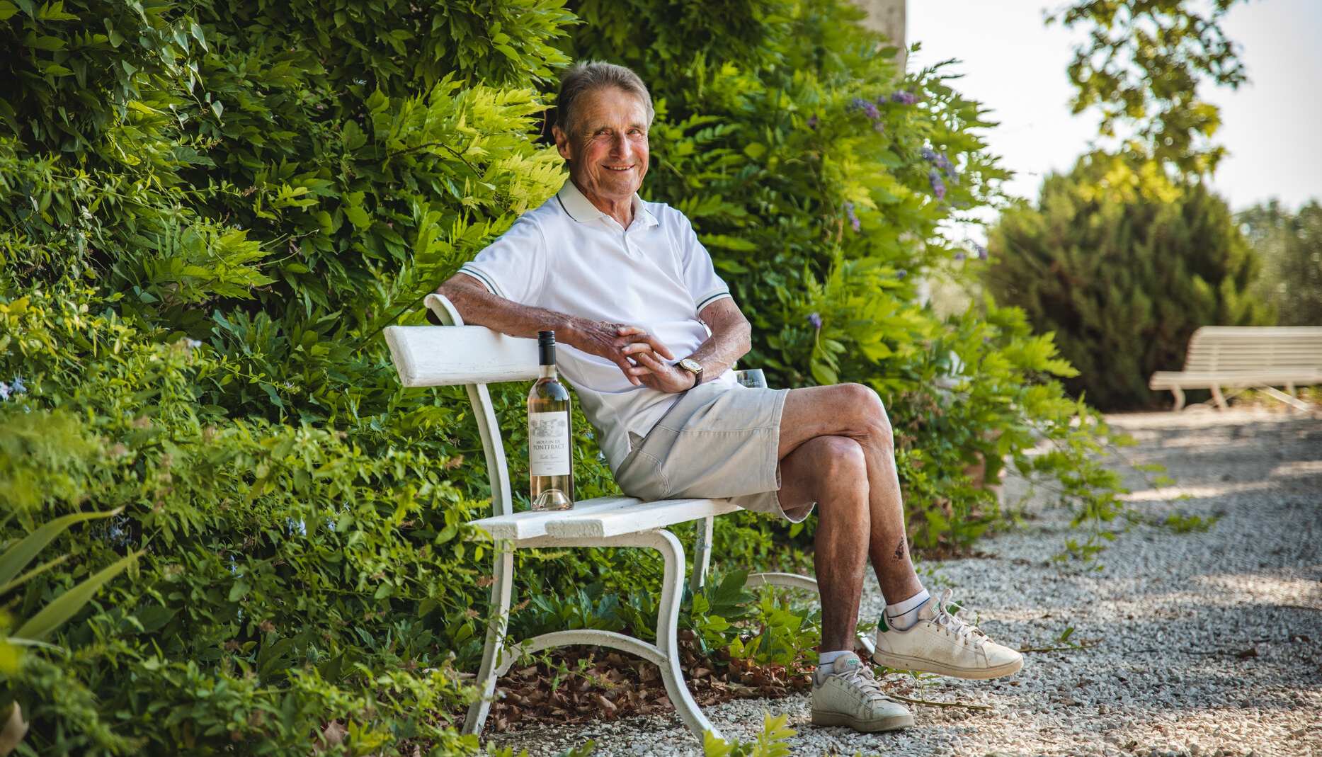Winemaker, Monsieur Paul, sits on a bench with his Provence rosé wine