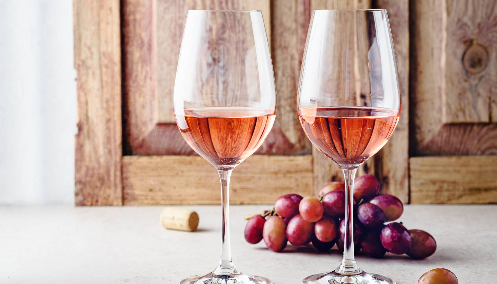 Dry rosé wine - two glasses of rosé wine on a table with red grapes in the background