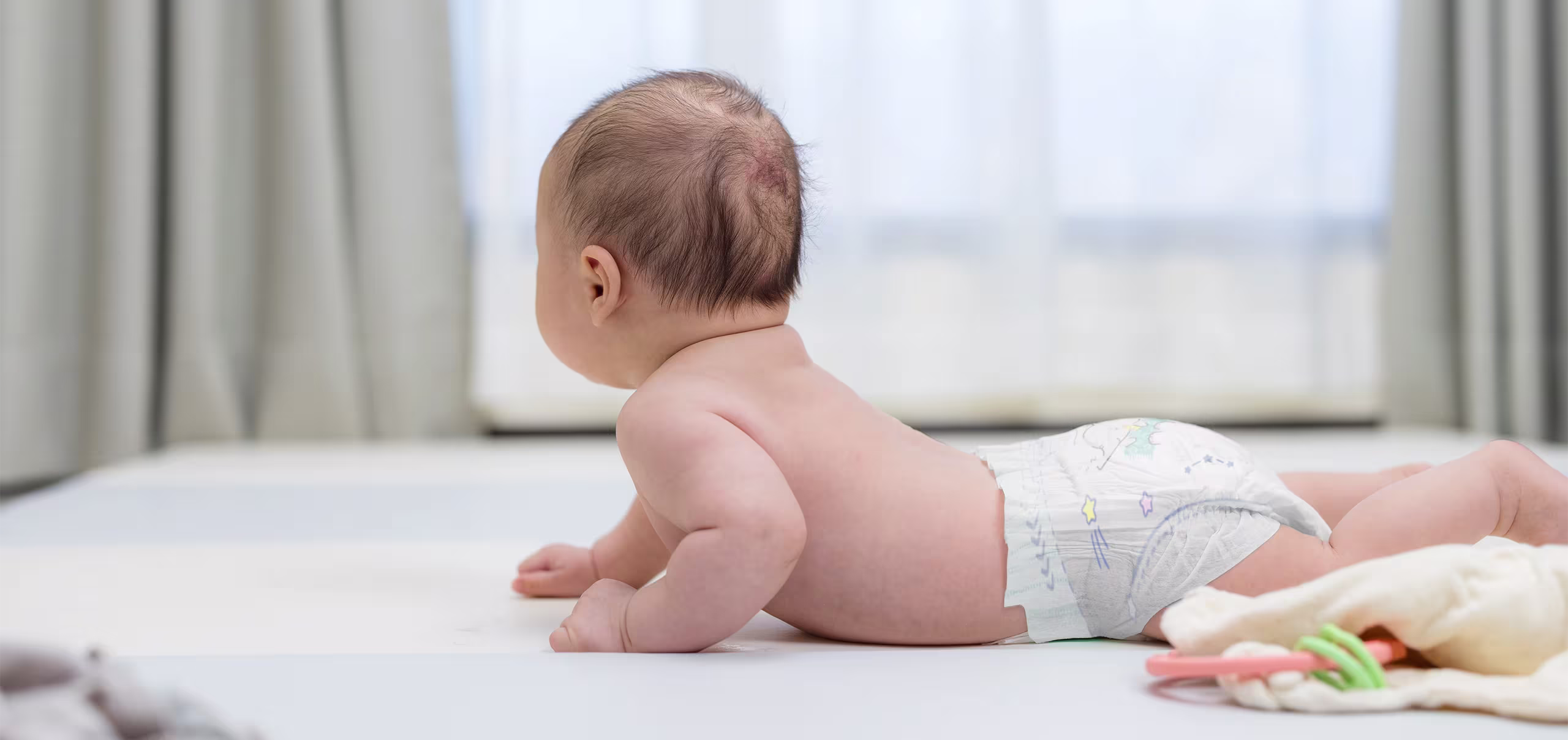 Un bebé recién nacido acostado boca abajo en una cama, con pañales Pampers