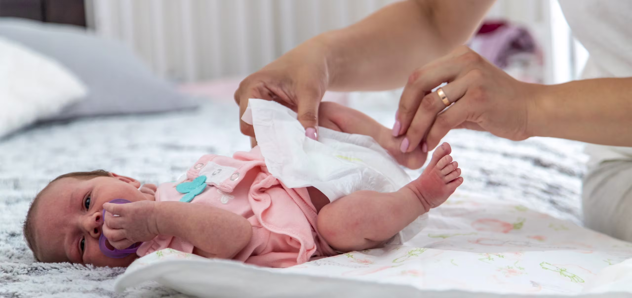 Manos de una madre colocando un pañal suave y cómodo a su bebé recién nacido acostado en la cama, representando la protección e higiene diaria.