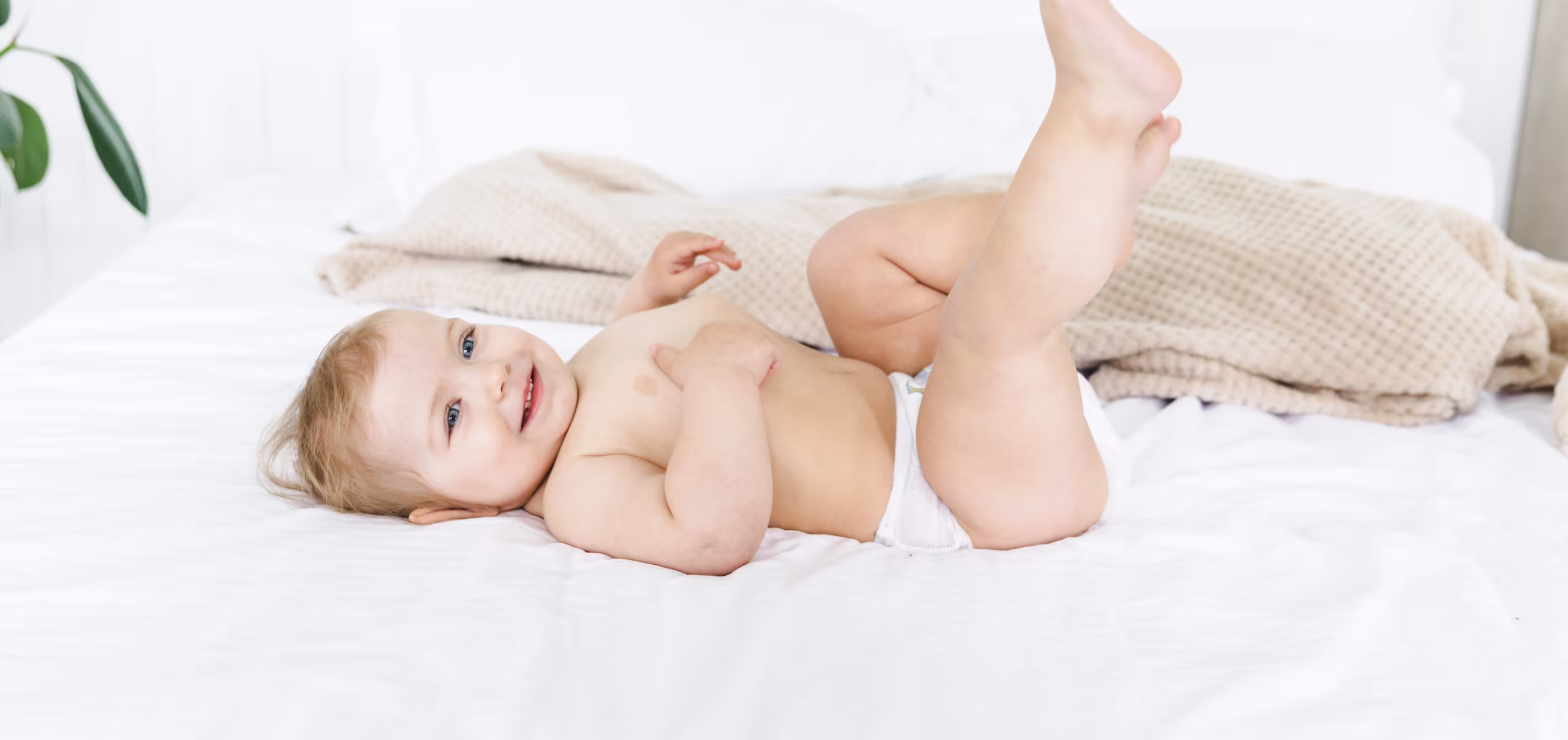 Bebé sonriente apoyado boca abajo sobre una cama con sábanas blancas.