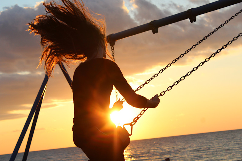 Women on swing in front of sun
