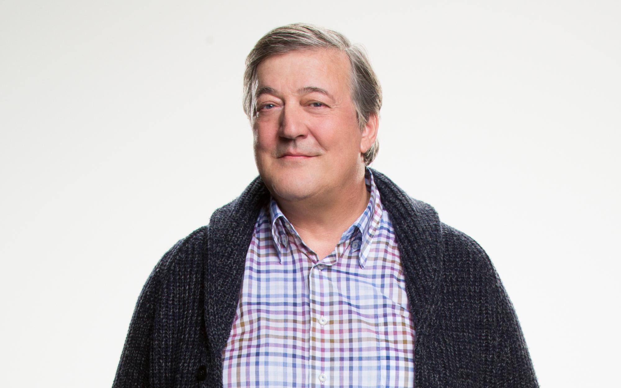 Stephen Fry smiling and wearing a checkered shirt and cardigan