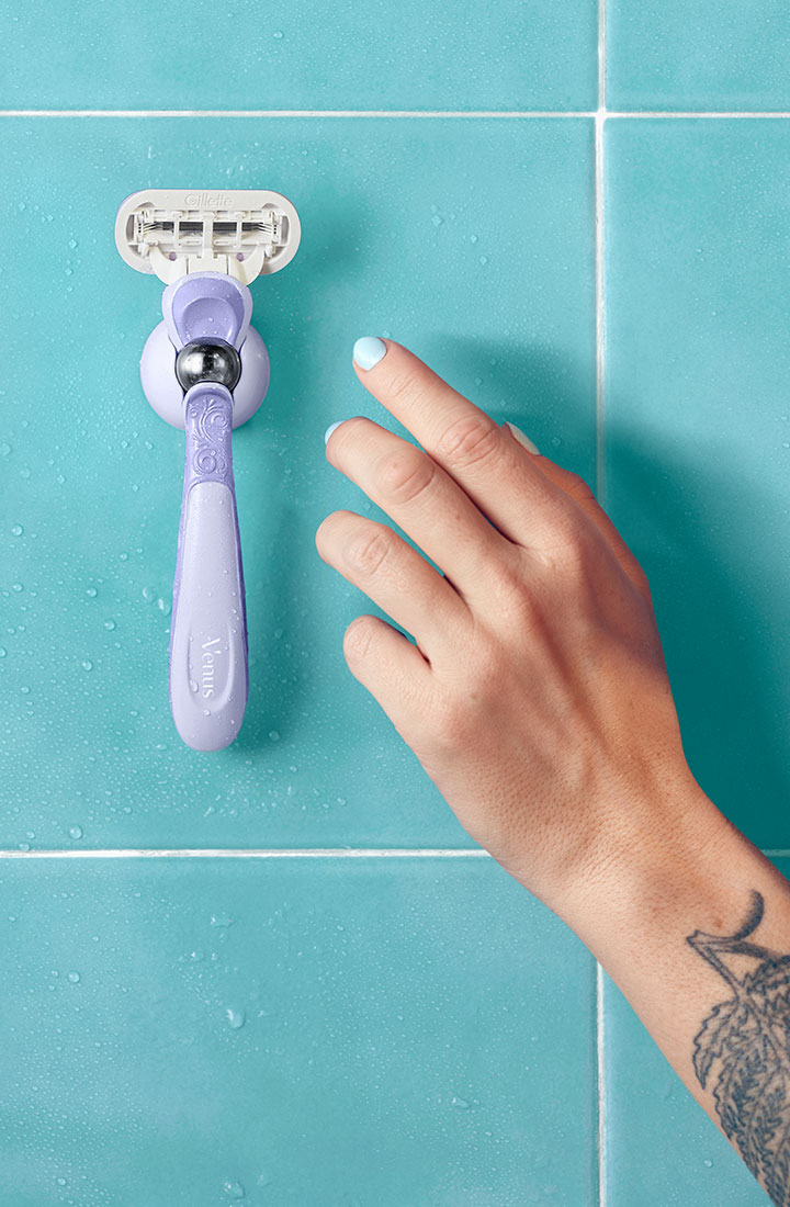 Hand streckt die Hand aus, um den Extra Smooth Rasierer zu nehmen, der an der Duschhalterung an der Wand befestigt ist
