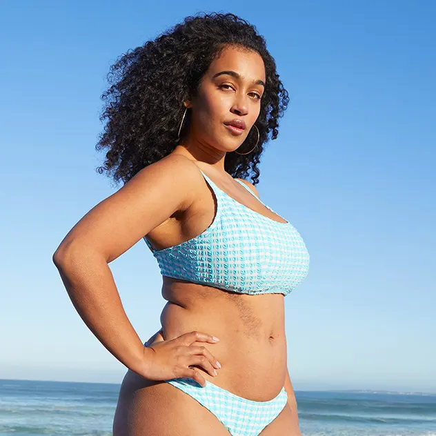 Curly haired woman in a blue bikini posing at the beach