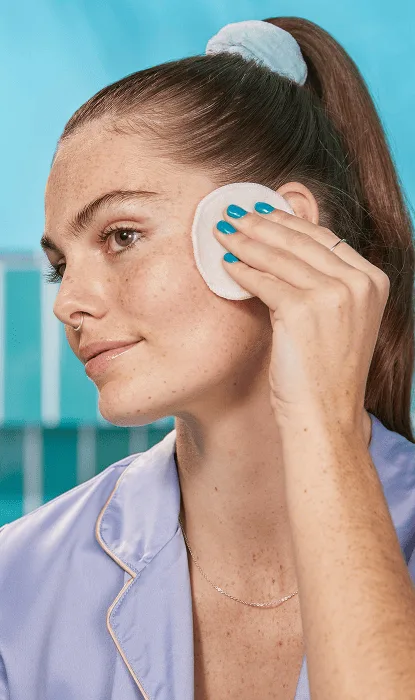 Young woman in the bathroom cleans her cheek with a cotton pad