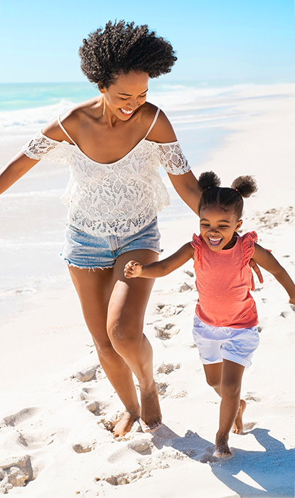 Mother and daughter laughing and running on the sandy beach