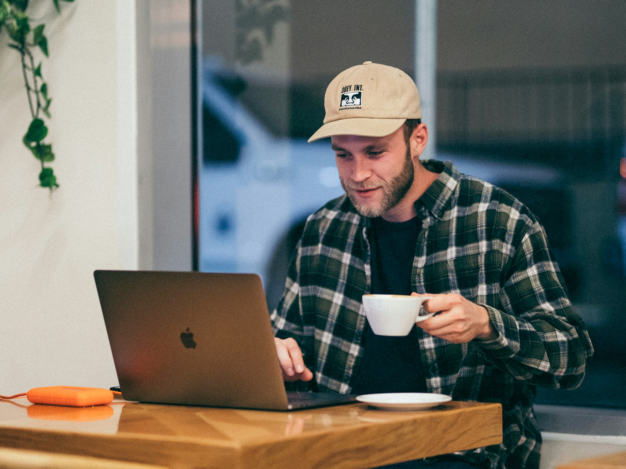 Ein Mann sitzt mit Kaffeetasse am Tisch vor seinem Laptop.
