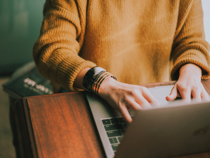 A women sittting and writing on her laptop.