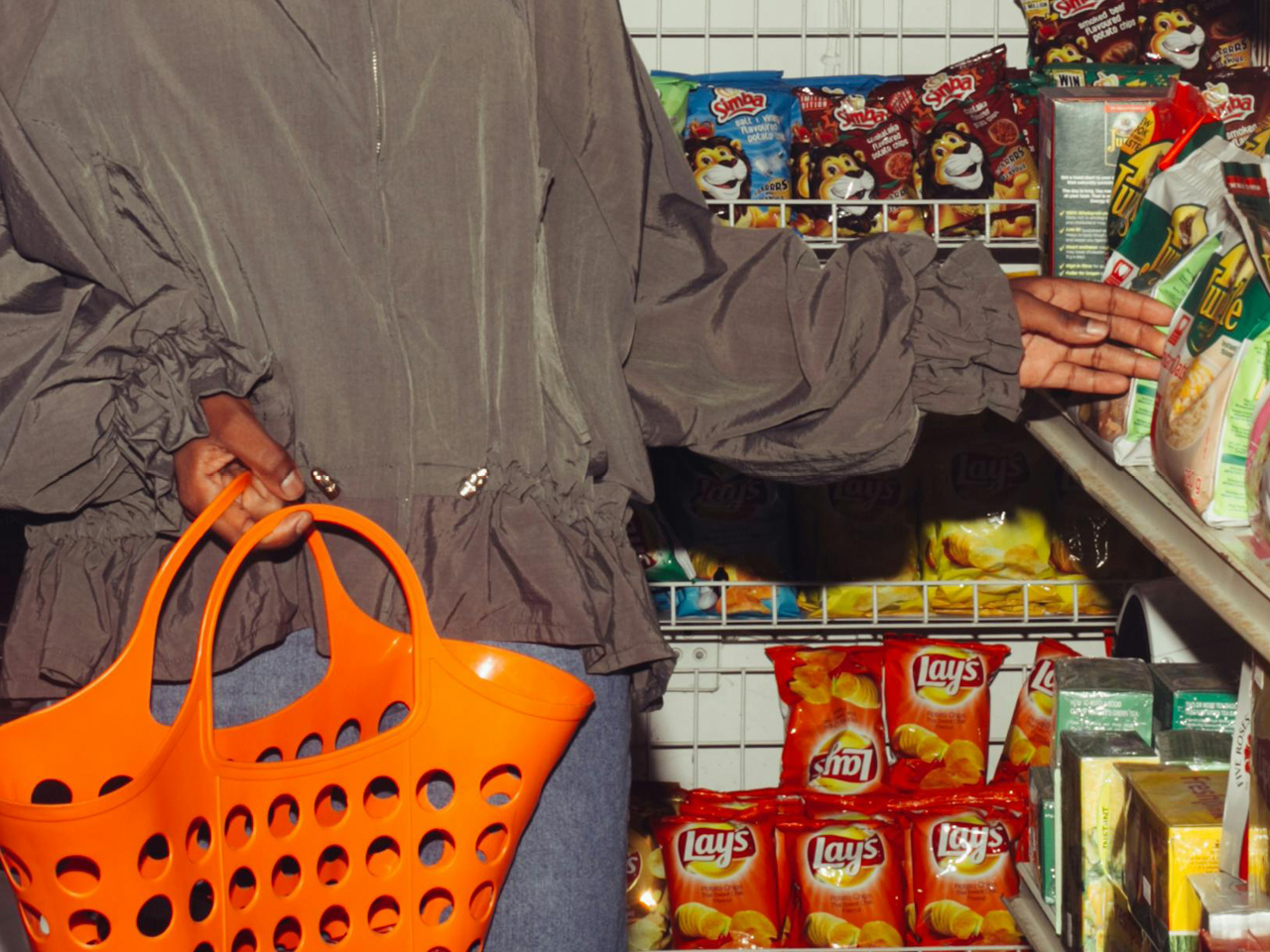 Eine Person steht mit einer Einkaufstasche vor einem Supermarktregal und greift nach einer Chipstüte.