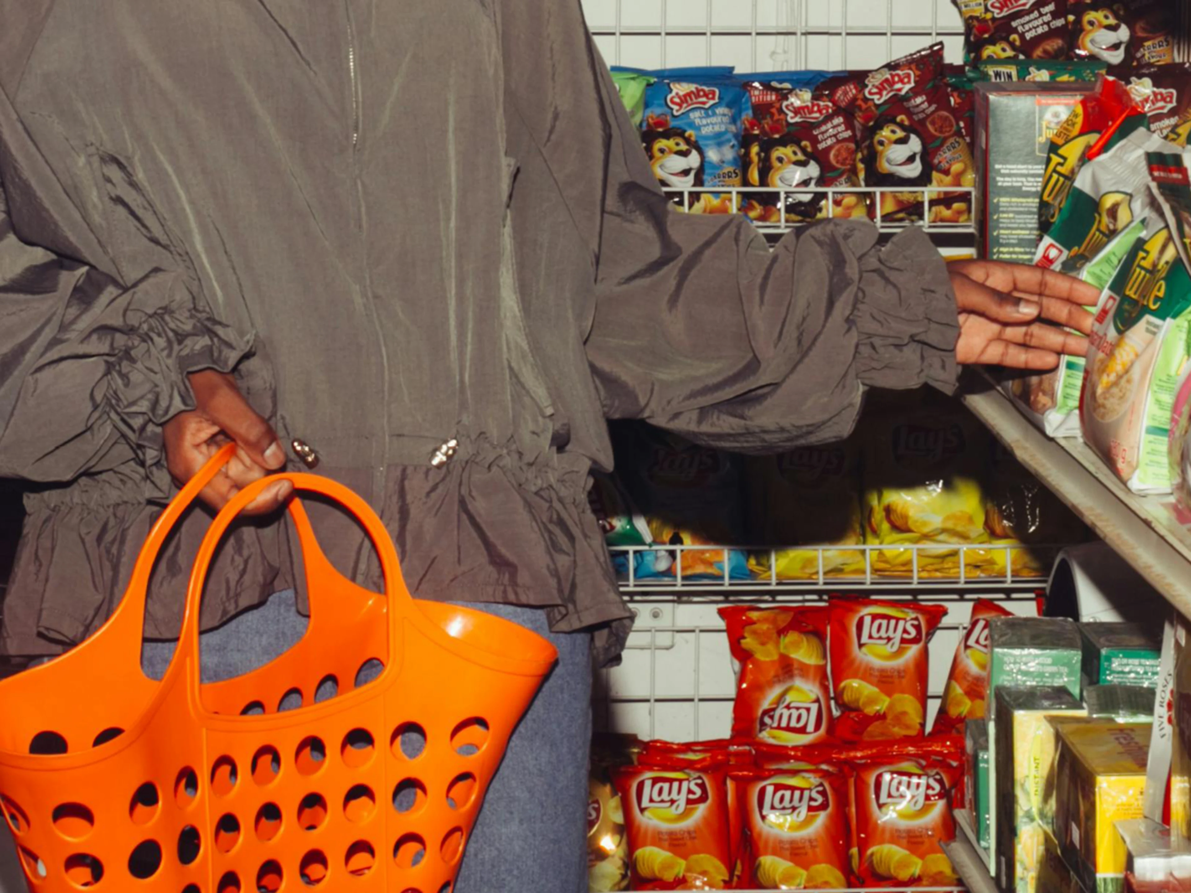 Eine Person steht mit einer Einkaufstasche vor einem Supermarktregal und greift nach einer Chipstüte.