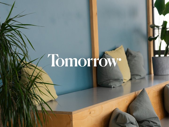 Eine gemütliche Ecke im Tomorrow Office mit Sitzbänken und Kissen. Im Vordergrund steht das Tomorrow Logo.