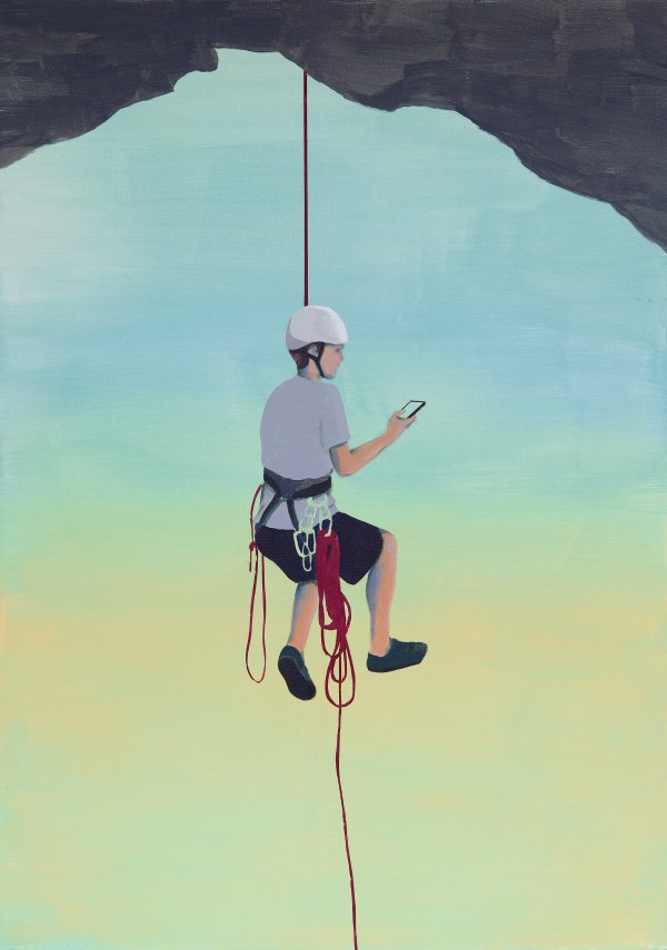 Ein Kletterer hängt am Seil und blickt auf sein Smartphone
