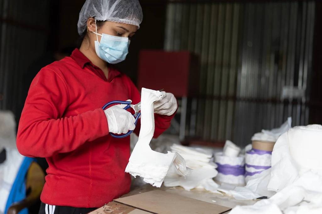 The picture shows the production process for sustainable sanitary pads. A woman cuts the banana fibers to size.