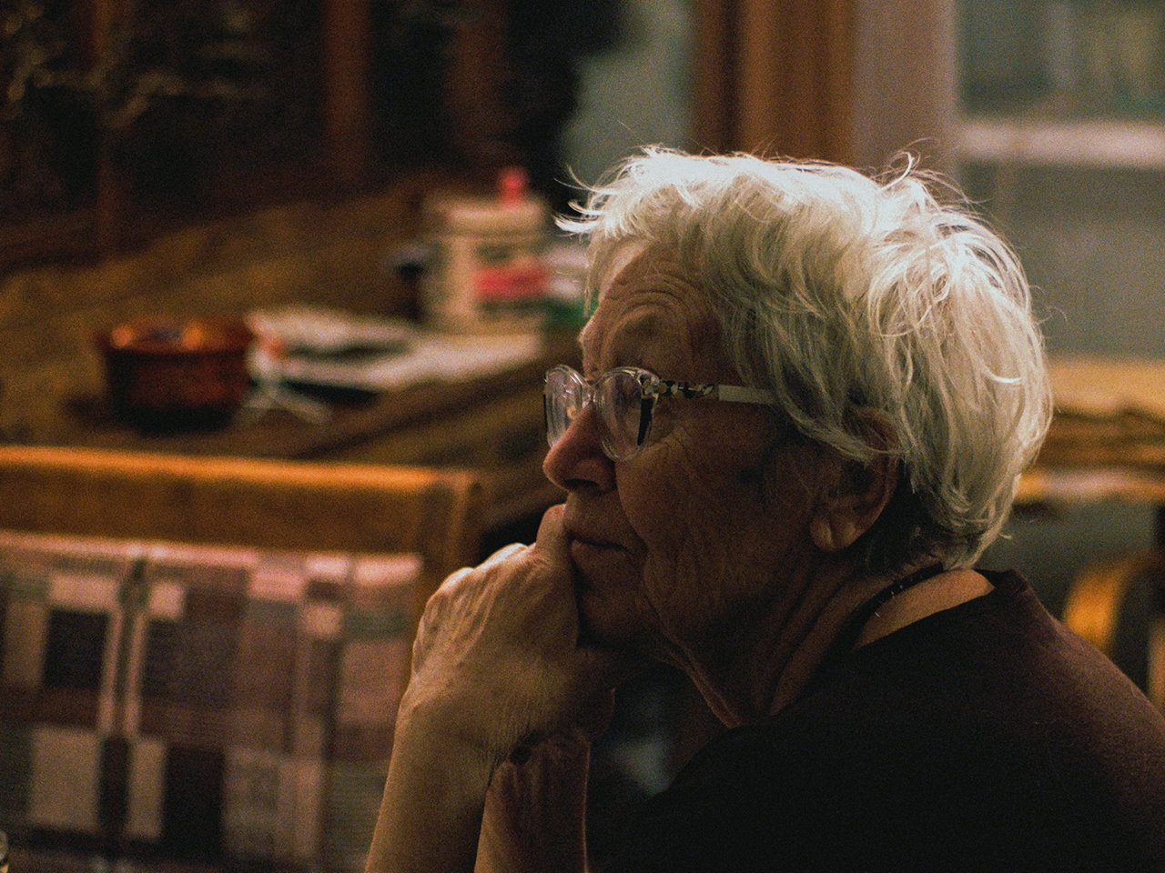 An elderly woman sitting in a room. She looks a bit concerned. 