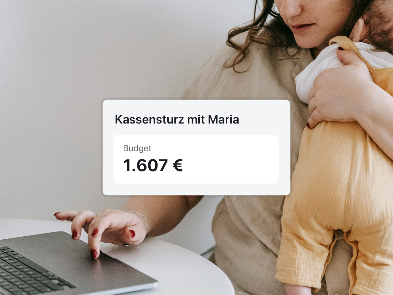 Eine Frau arbeitet am Laptop mit einem Baby im Arm.