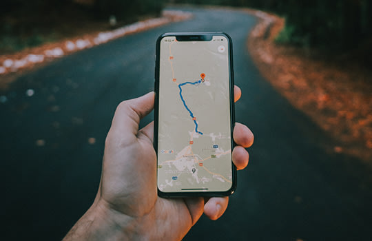 Fotografie, bei der die Hand einer Person auf einem geschlungenen Weg ein Handy mit einer Navigationsapp hält. 