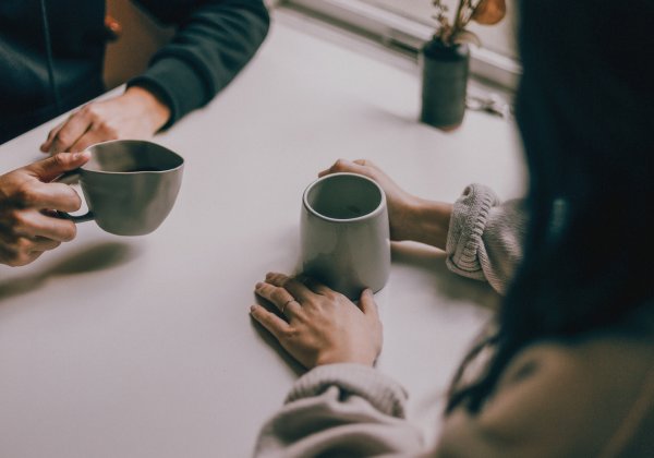 A couple sits together on a table, you can see just their hands and a cup of tea.