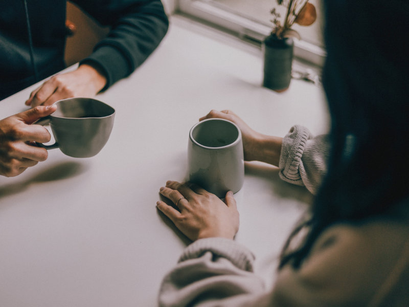 A couple sits together on a table, you can see just their hands and a cup of tea.