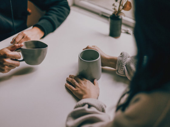 Ein Paar sitzt gemeinsam am Tisch. Zu sehen sind die Hände, ihre Hände halten jeweils eine Tasse Tee oder Kaffee.