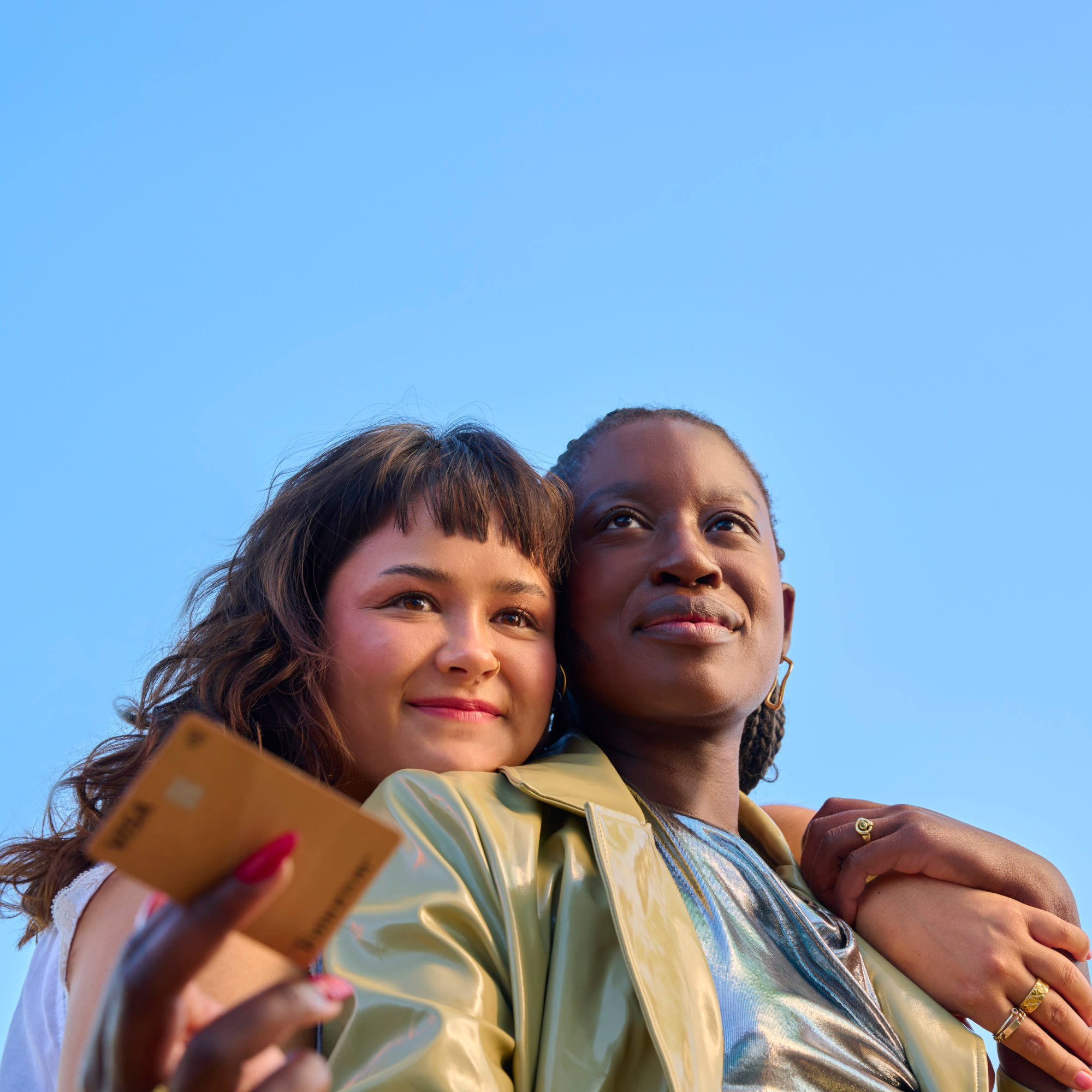 Two young women embrace each other, one holding a Tomorrow Card in her hand.