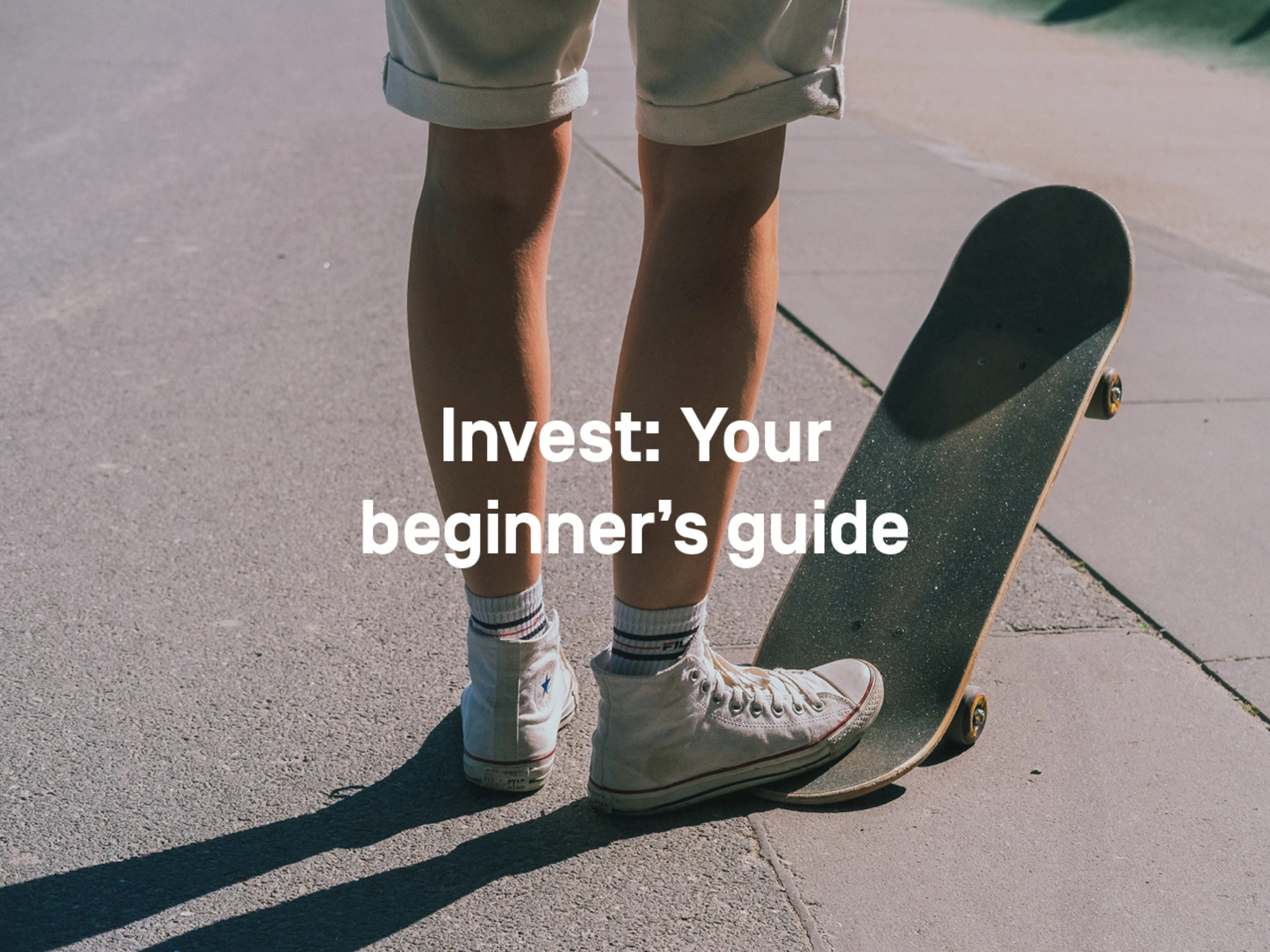 A young man in shorts and Chucks stands on the street. His right foot is on the back of a skateboard, the front wheels are in the air.
Text: Invest: Your beginner's Guide