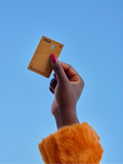 Eine Person hält eine Hand mit der hölzernen Tomorrow Card in Richtung des blauen Himmels.