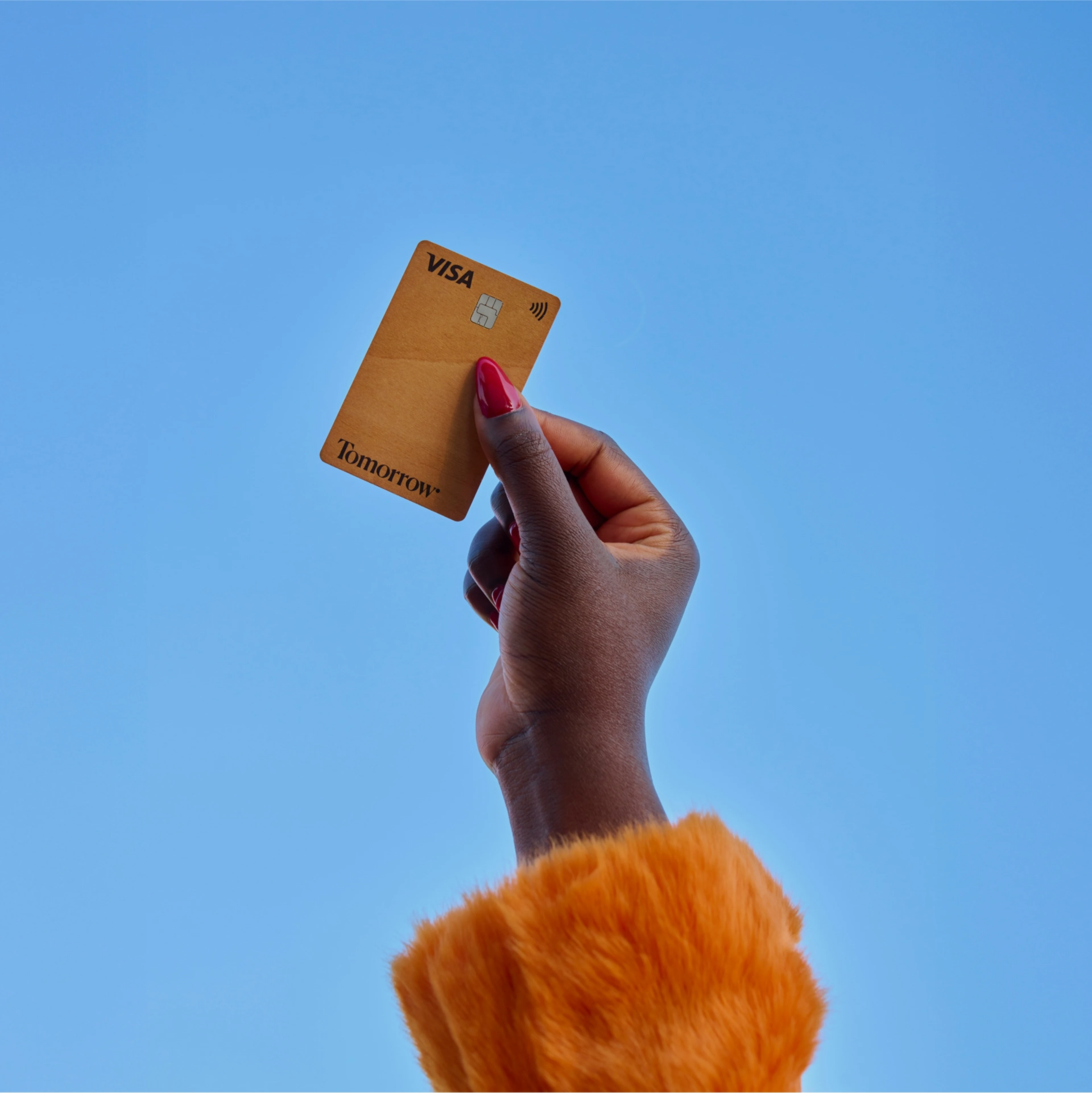 Eine Person hält eine Hand mit der hölzernen Tomorrow Card in Richtung des blauen Himmels.