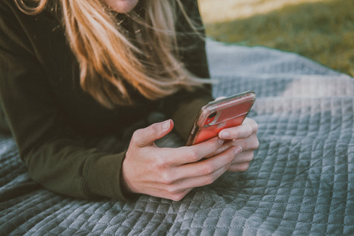 Eine Frau auf einer Picknickdecke hält ein Smartphone in beiden Händen