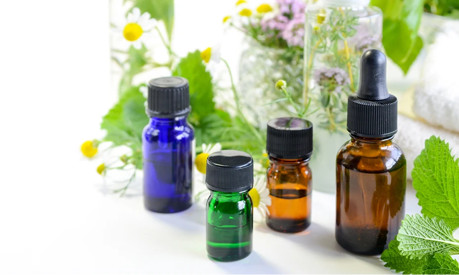Small glass bottles of oils in different colors with a black cap surrounded by fresh daises on a white background