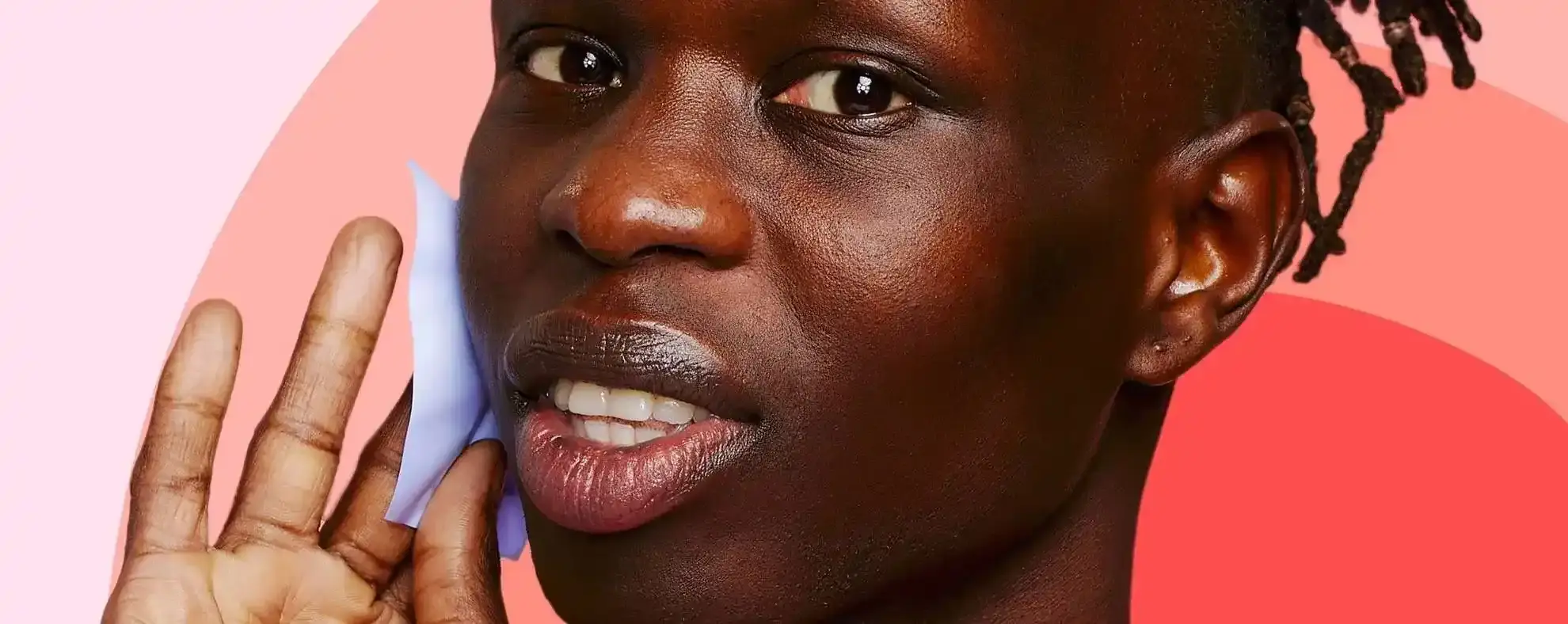 A person holds a blue object against their cheek, set against a background of pink and red gradient shapes.