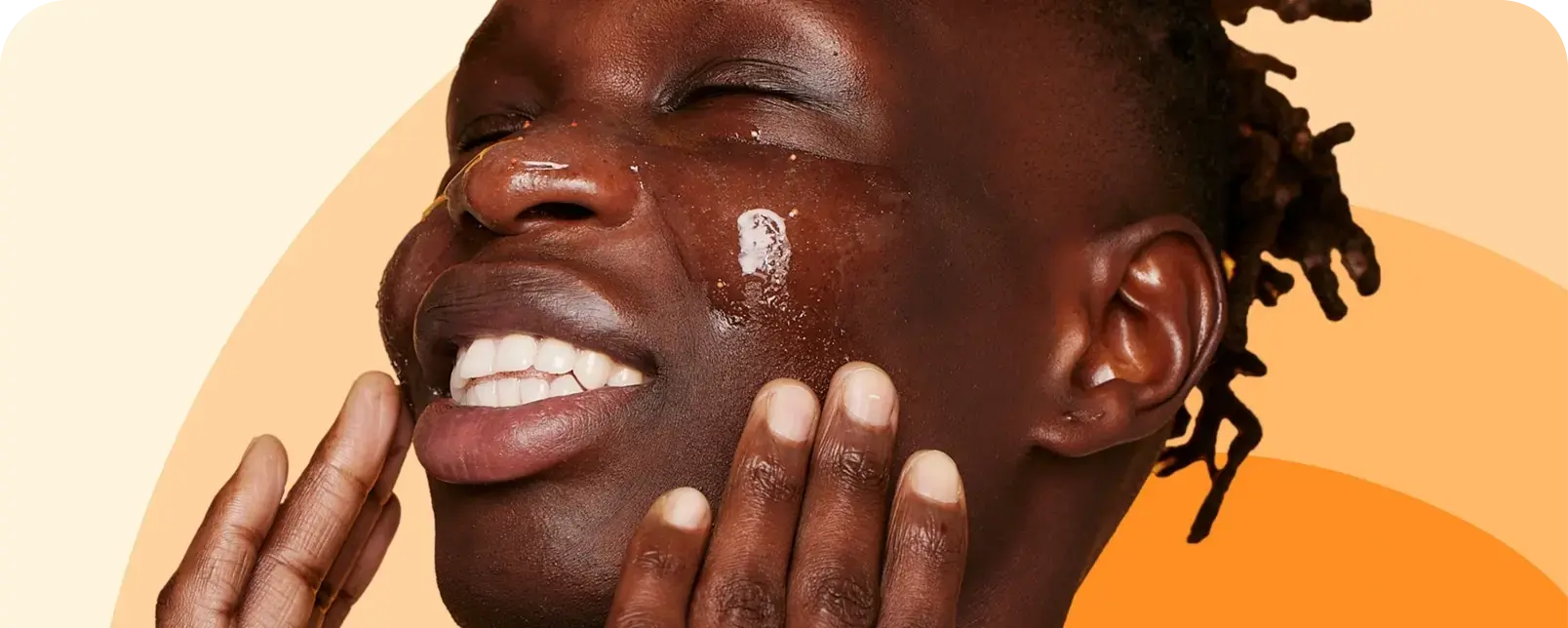 A person smiles with eyes closed, applying a glossy skincare product on their face, using their hands. The background features a gradient of light to dark orange hues.