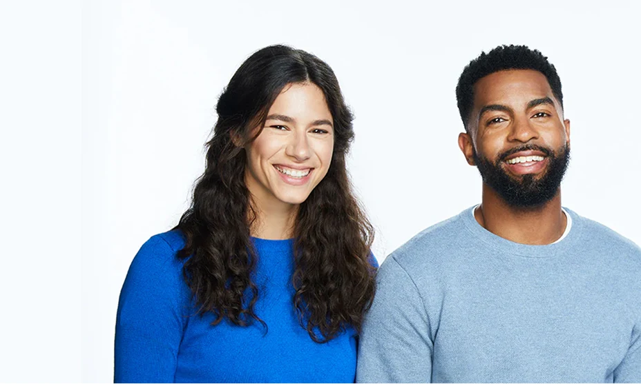 Woman with long brown hair smiling next to two men with dark hair wearing long sleeve shirts on a white background.