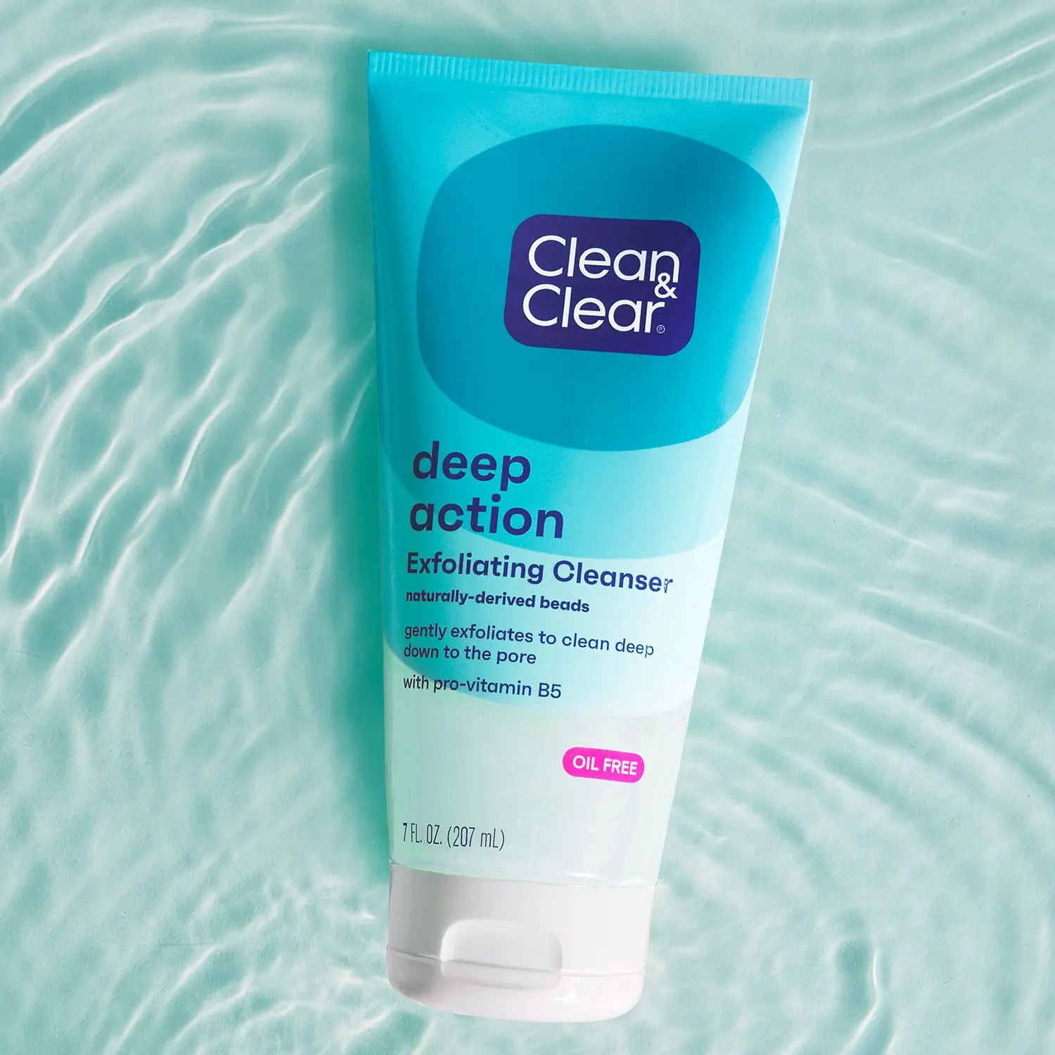 A turquoise tube labeled "Clean & Clear deep action Exfoliating Cleanser" with text: "naturally-derived beads, gently exfoliates to clean deep down to the pore, with pro-vitamin B5, OIL FREE, 7 FL OZ (207 mL)" rests on rippling water.