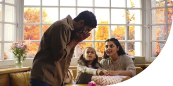 Man sneezing in front of his wife and little daughter while they wrap presents