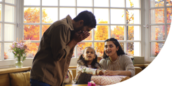 Man sneezing in front of his wife and little daughter while they wrap presents